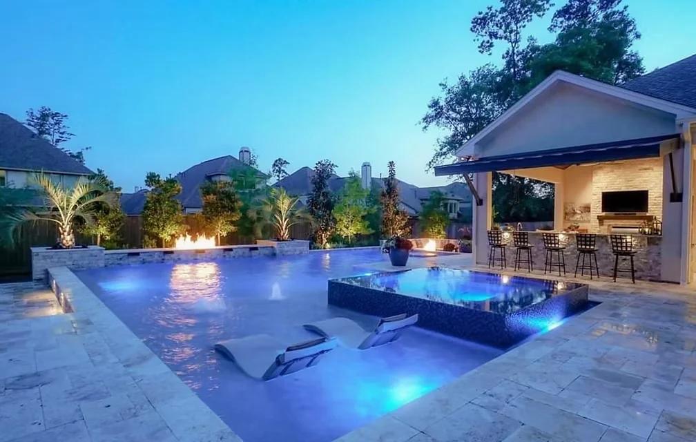 Luxury custom pool with integrated spa, fire bowls, and outdoor kitchen bar at dusk in Houston