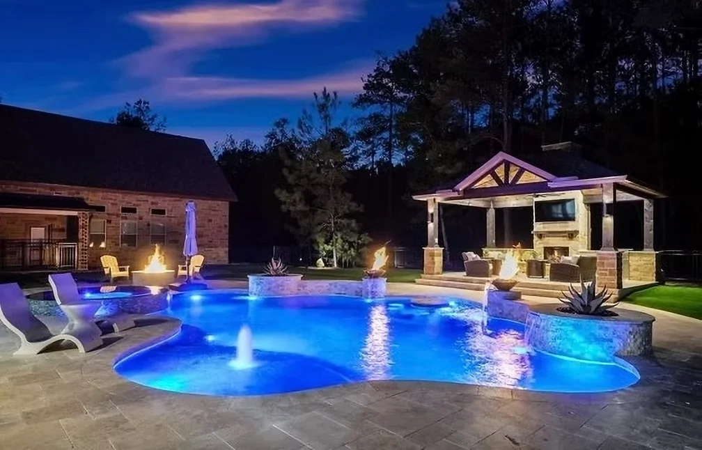 Resort-style pool with blue LED lighting, fire features, and covered pavilion at night in Houston
